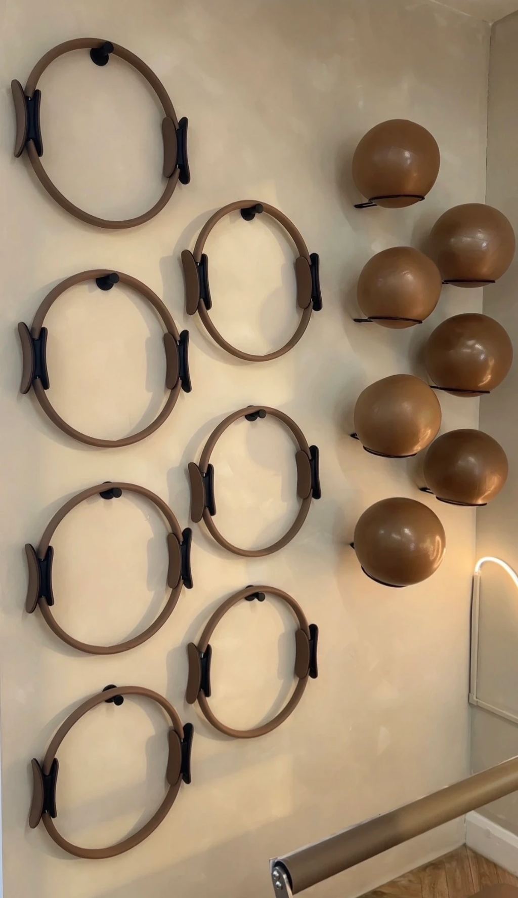Studio wall hung with Pilates rings and weighted balls in soft tan tones