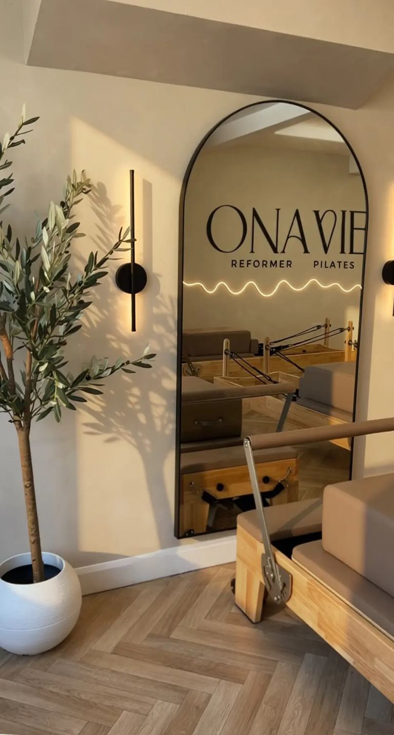 Arched mirror carrying the Onavie Reformer Pilates logo beside an olive tree