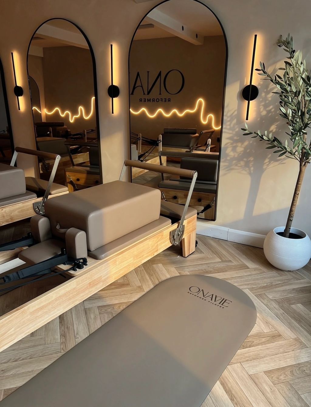 Reformer and branded Onavie mat in front of arched mirrors lit by a neon wave light