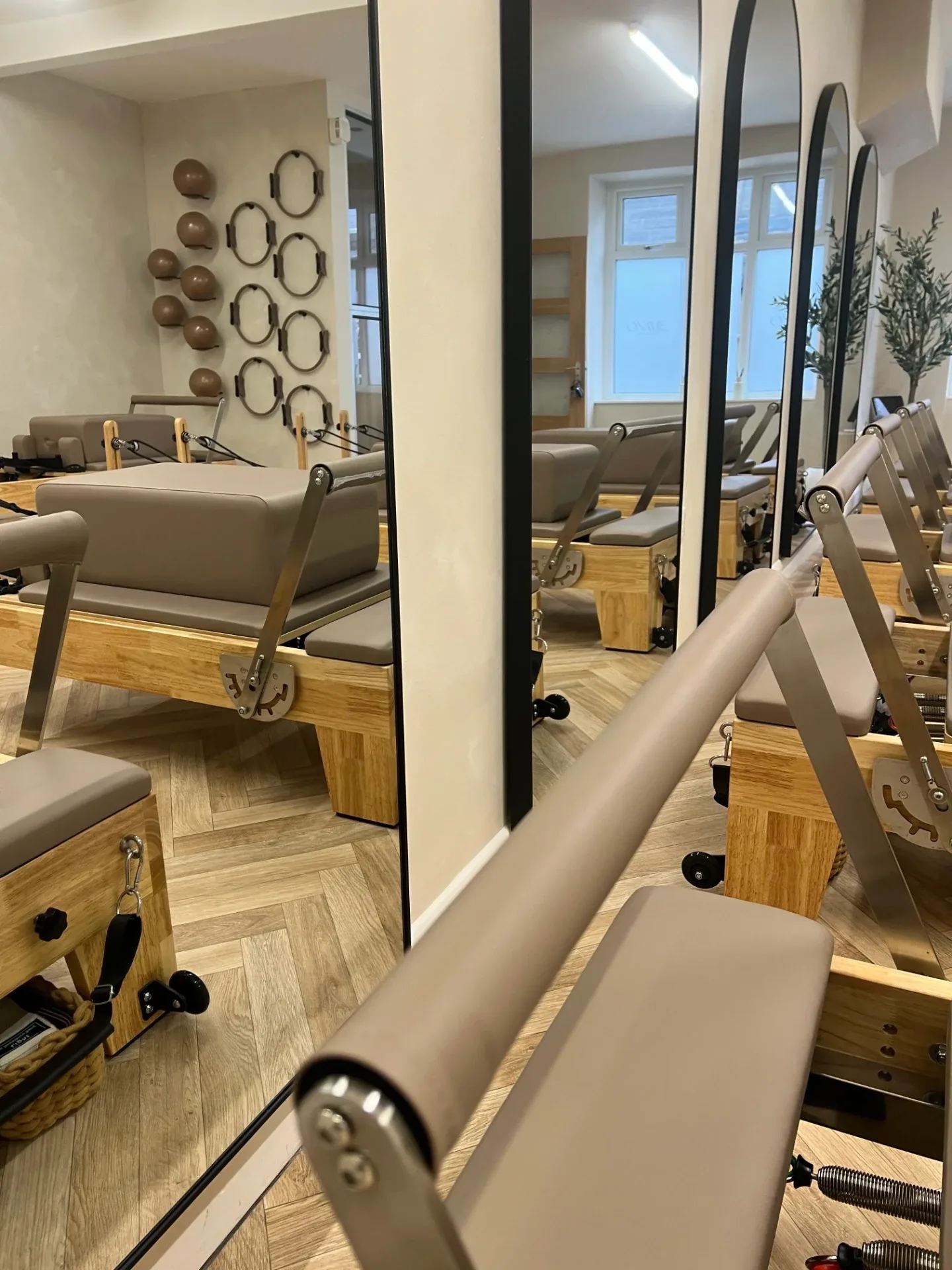 Reformer reflected in an arched mirror, with weighted balls and Pilates rings on the wall behind